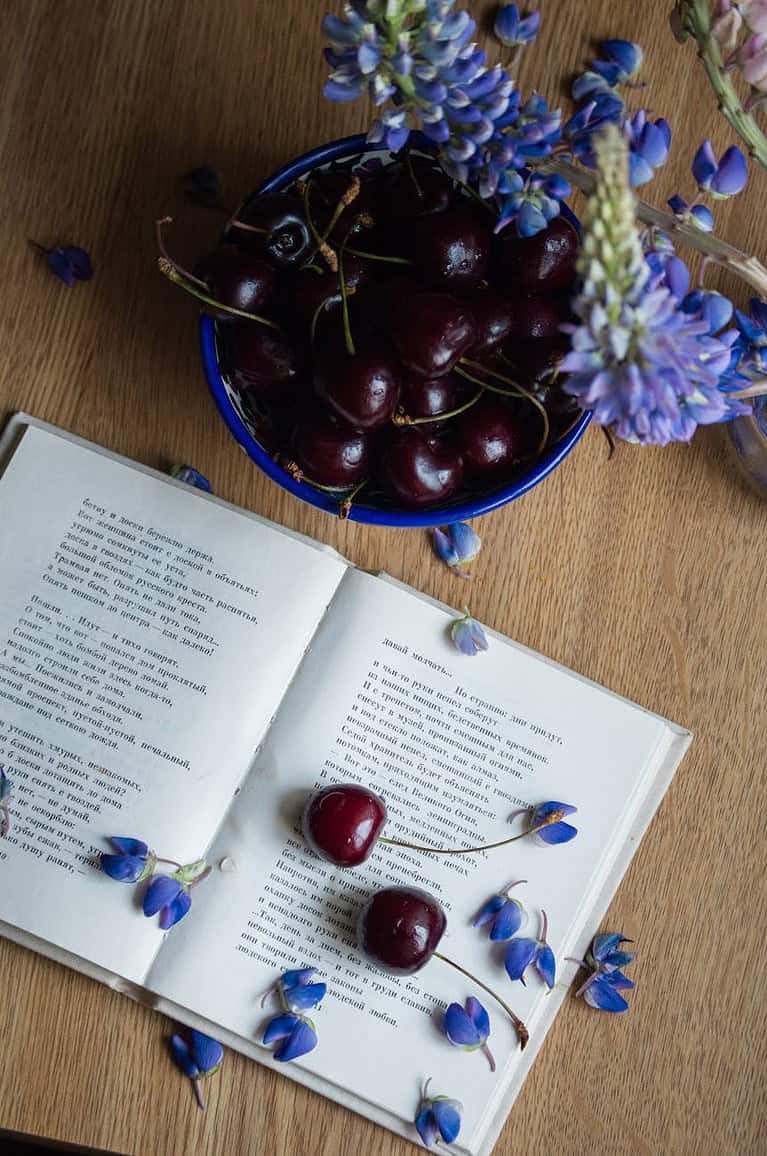 opened book placed on table with cherries and blue flowers