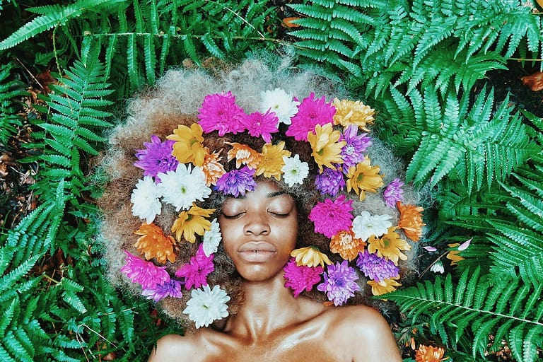 woman with floral headdress lying on green leaf plants