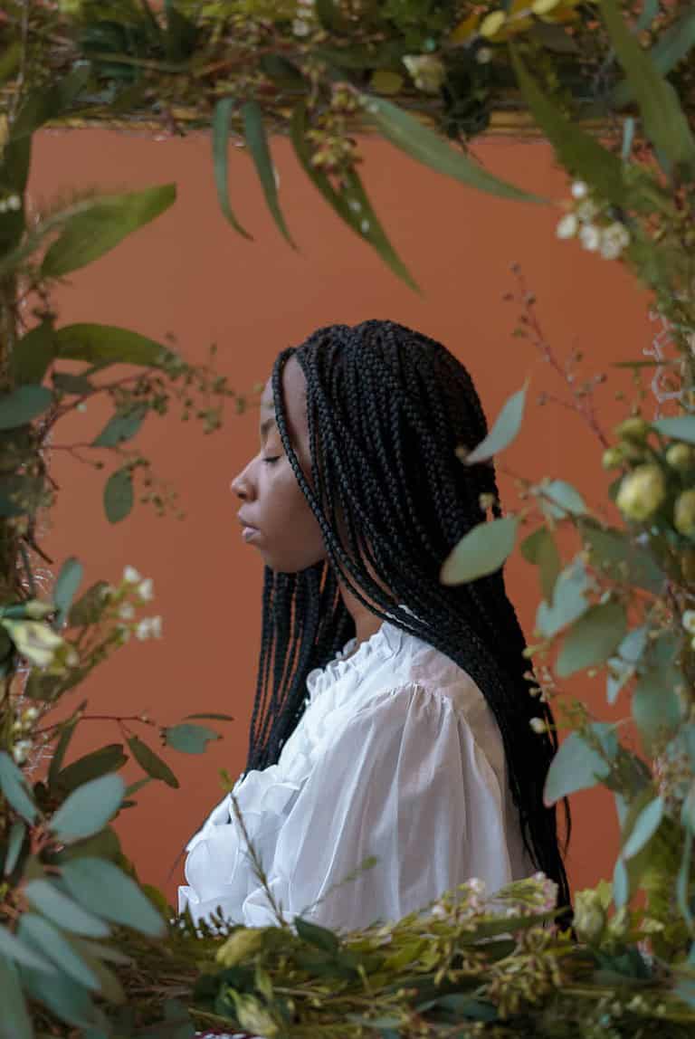 confident black lady with closed eyes near frame with plants
